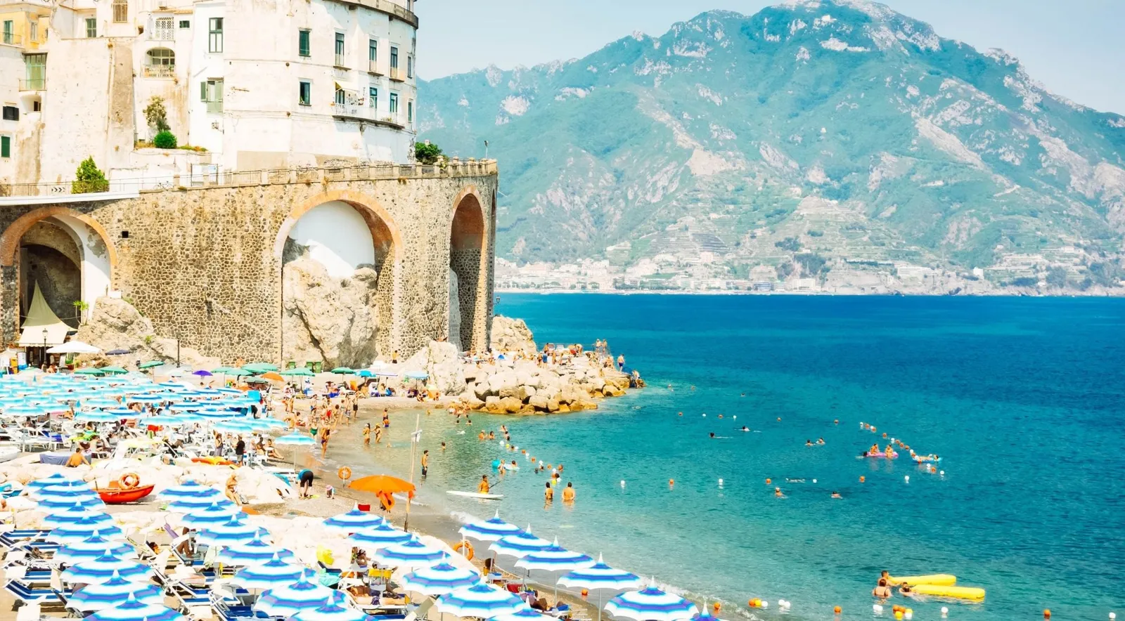 Beach umbrellas below the stone arches of Atrani on the Amalfi Coast