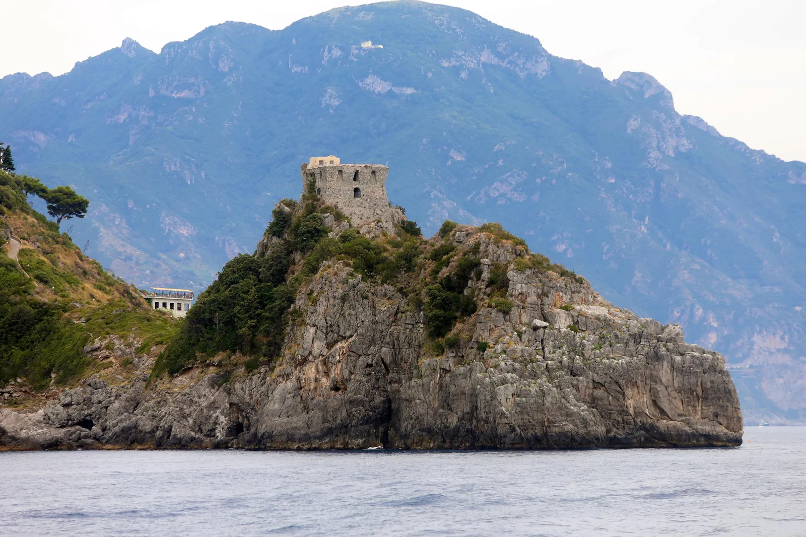 Rocky islet with a ruined stone watchtower on top, seen from the sea