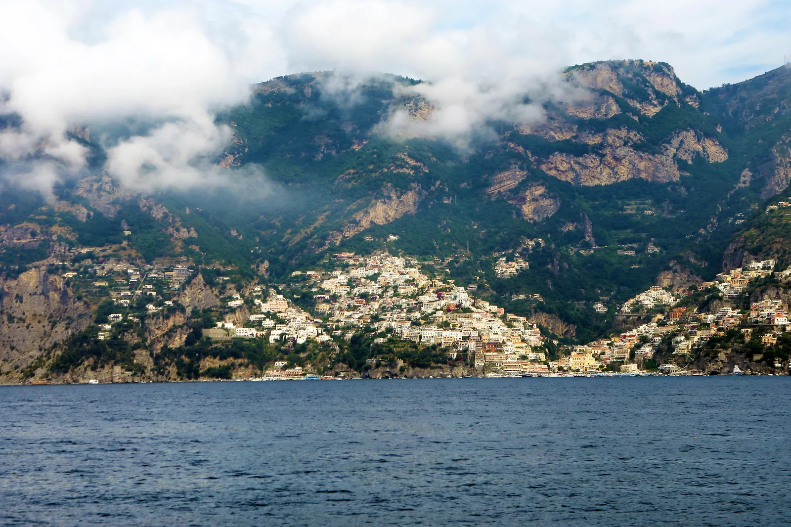 Positano's hillside houses below mountains and low cloud, seen from the water