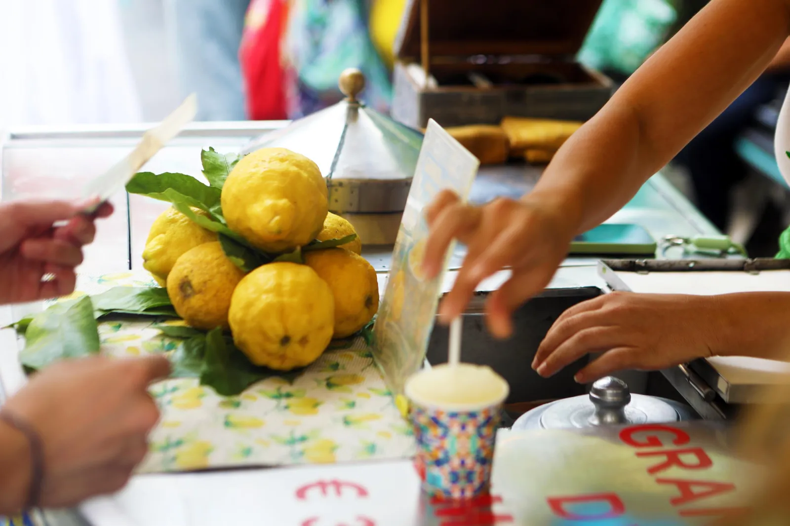 Whole lemons with leaves on a stall as hands serve a lemon ice