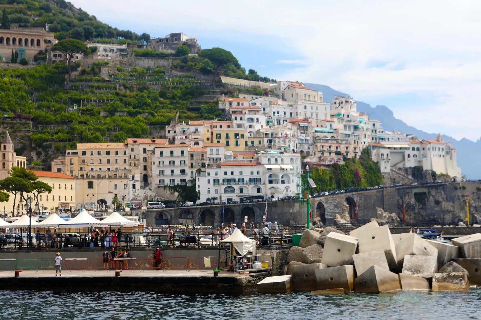 Amalfi's white buildings above a harbour wall with concrete blocks and the sea
