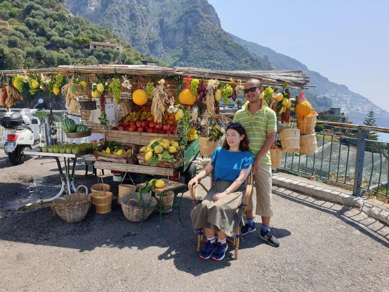 Couple posing beside a roadside fruit and lemon stall at a viewpoint over the mountains
