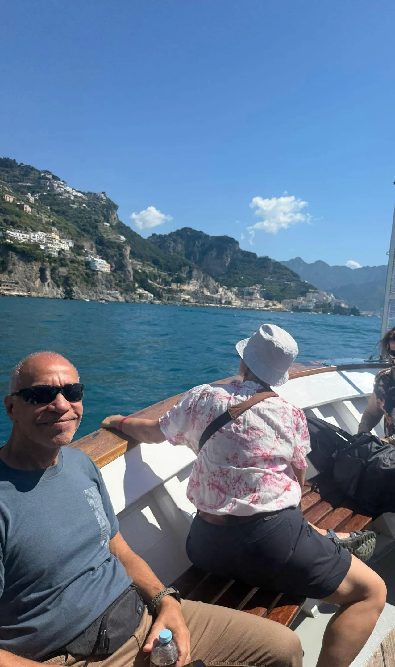 Two passengers seated on a boat with a rocky coastline across the water
