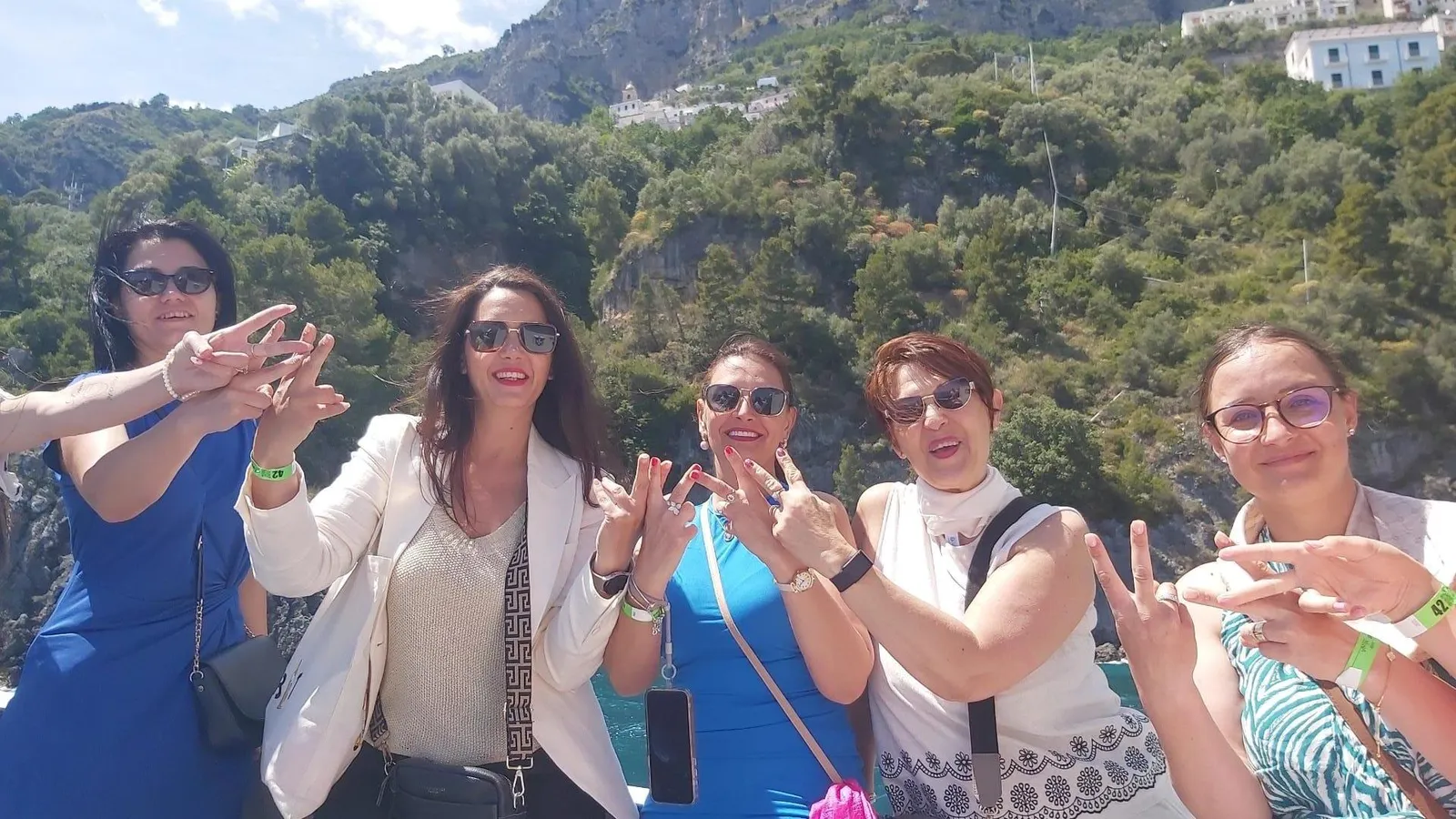 Five women posing with hand gestures in front of a wooded hillside