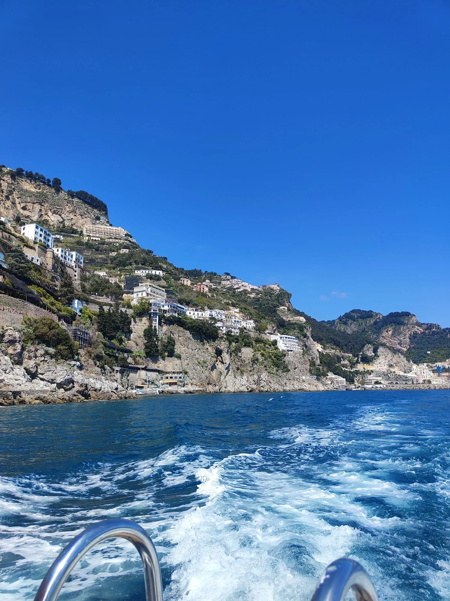 Boat wake on blue water with a cliffside coastline and houses behind