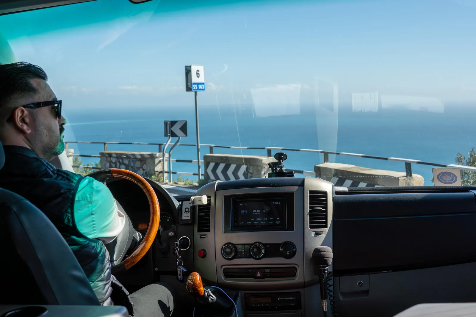 Driver at the wheel of a minibus on a coast road with the sea ahead