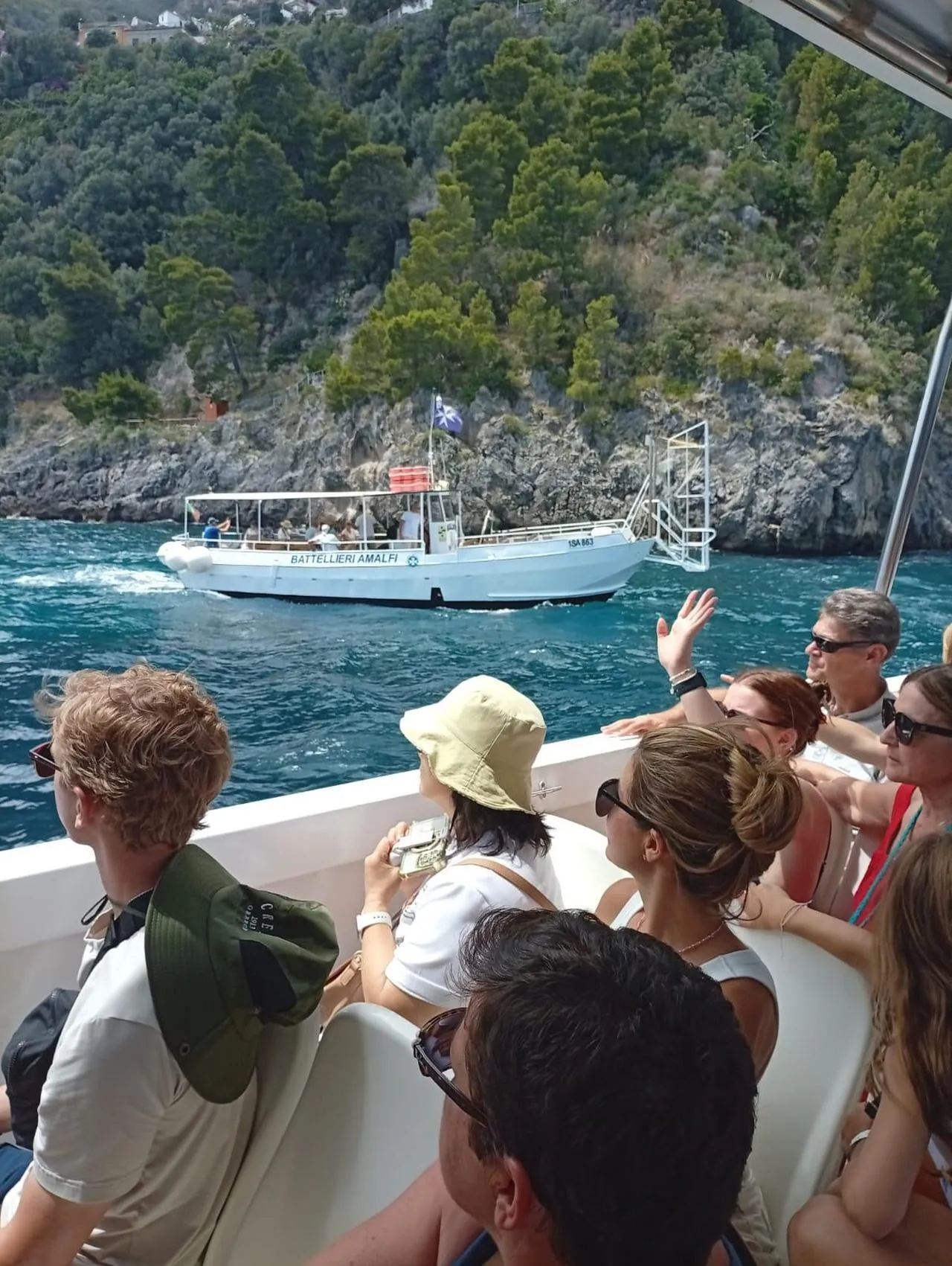 Passengers on a boat deck with a small white boat and a wooded rocky shore