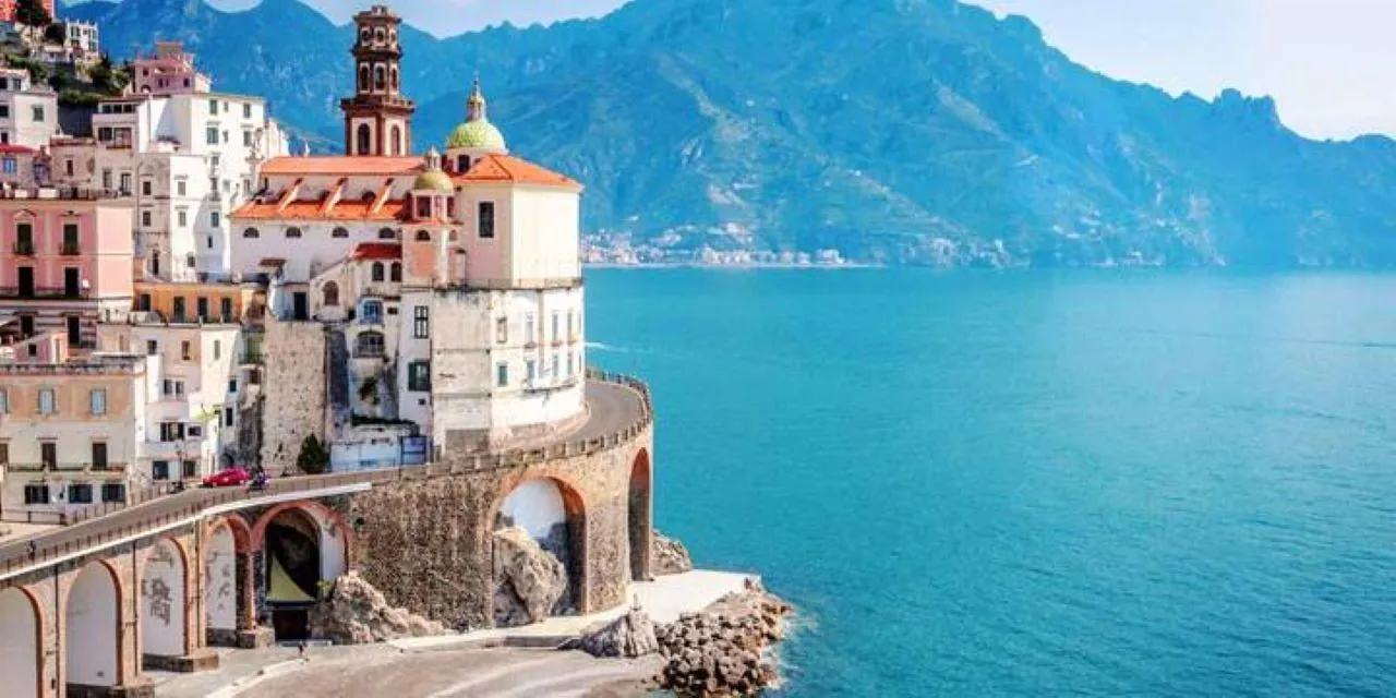 Atrani's pastel houses and church tower above a curved seafront road and turquoise water
