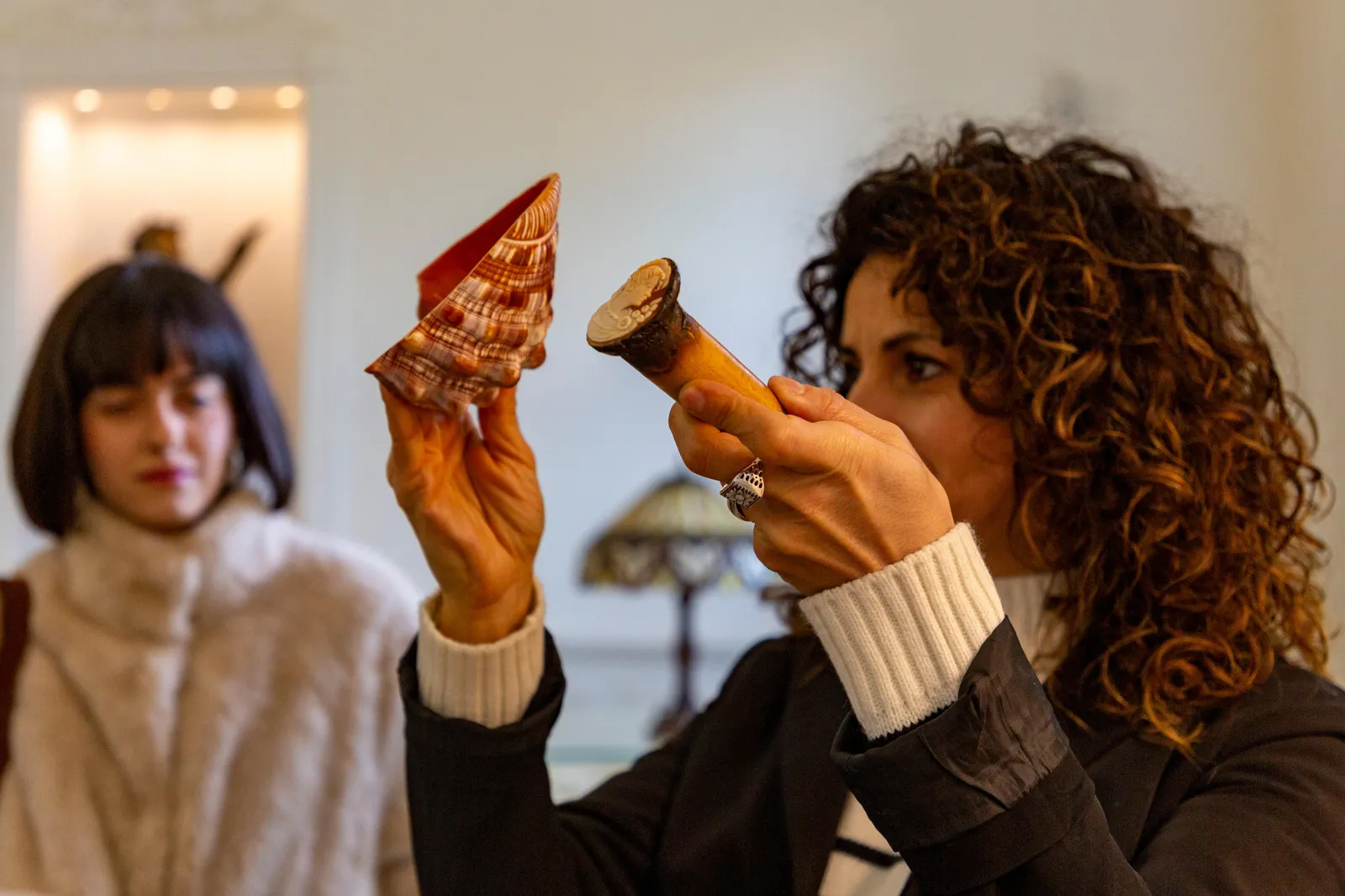 Woman holding up a carved shell to look at it in a shop, another woman behind