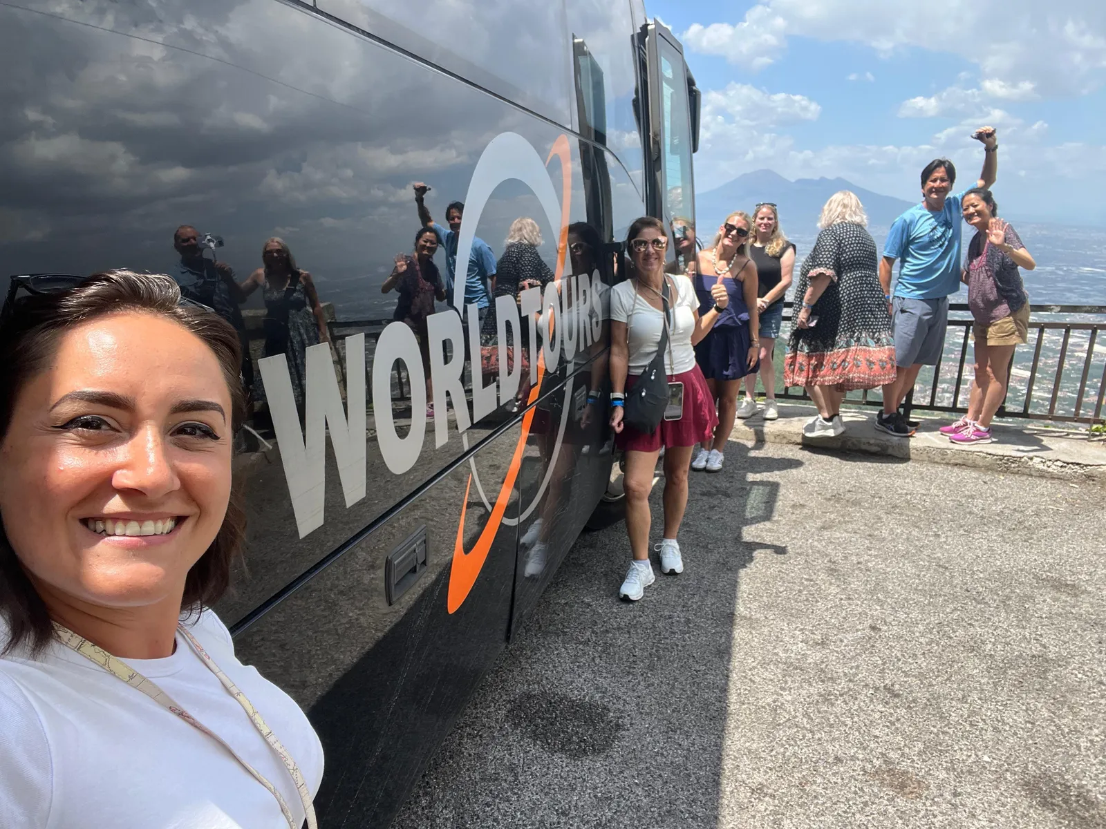 Woman smiling beside a coach while a group poses at a railing above the bay