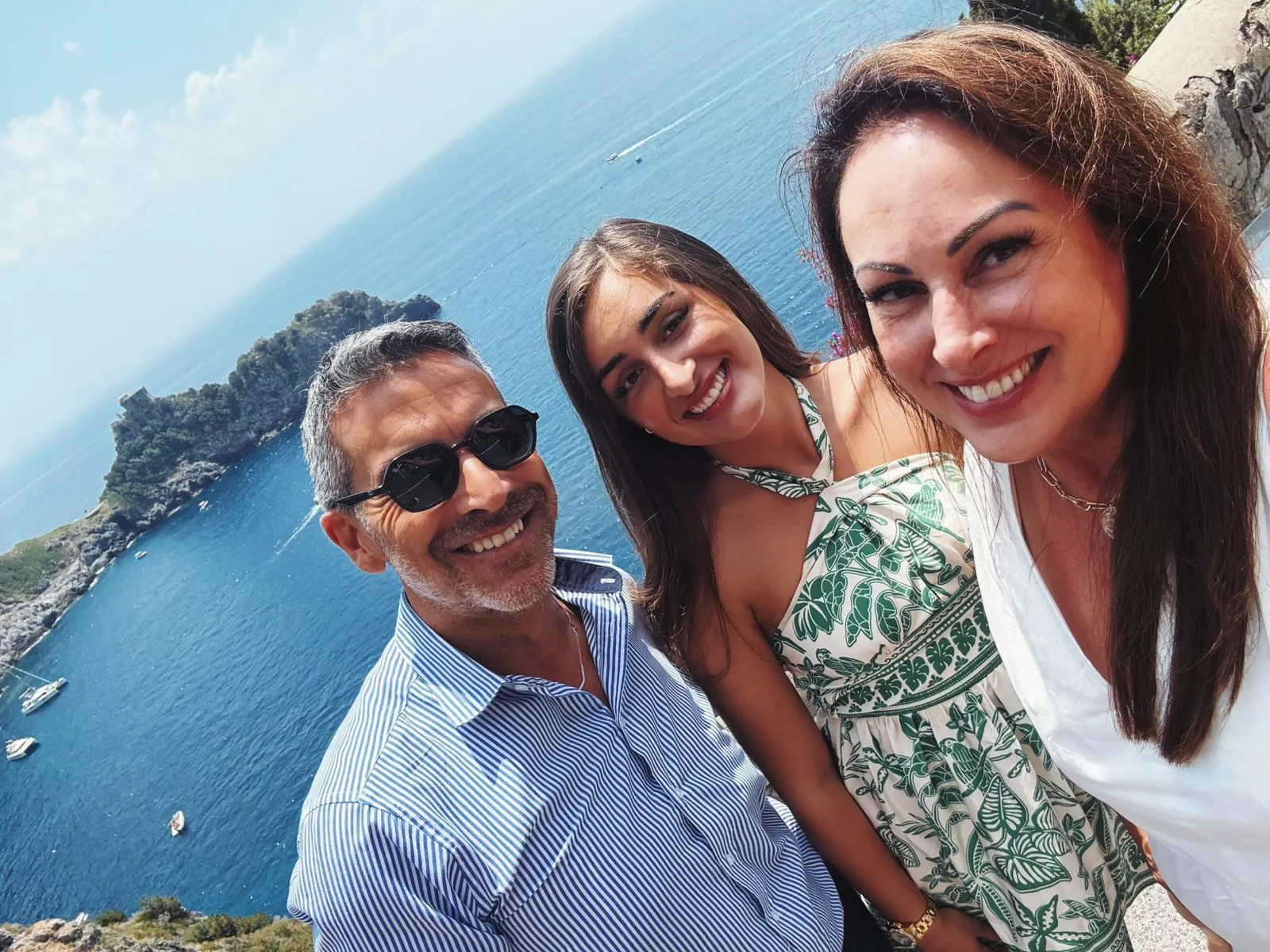 Three people posing for a selfie on a headland above blue water and a rocky islet