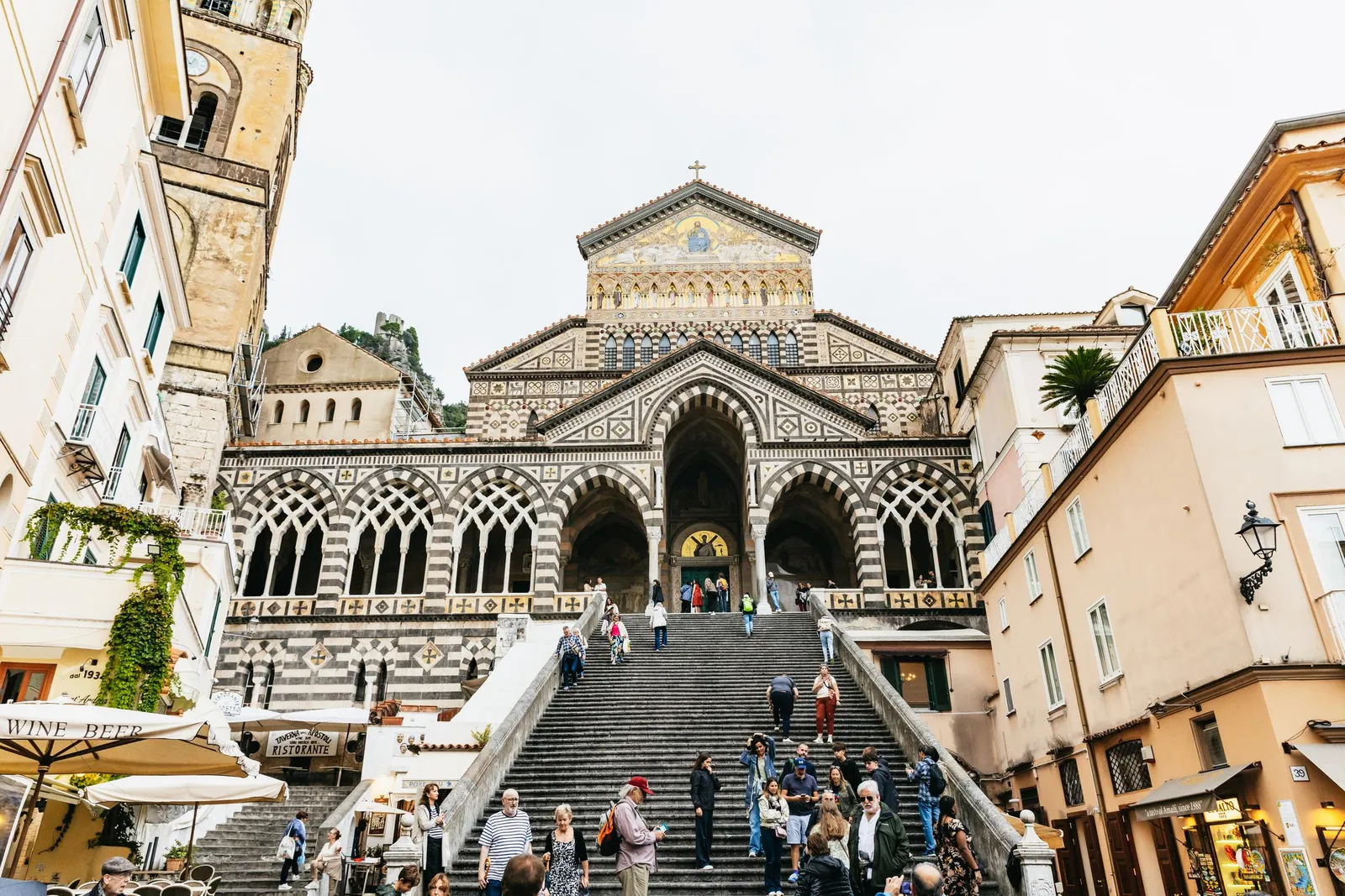 Amalfi cathedral's striped facade at the top of a wide stairway, with visitors on the steps