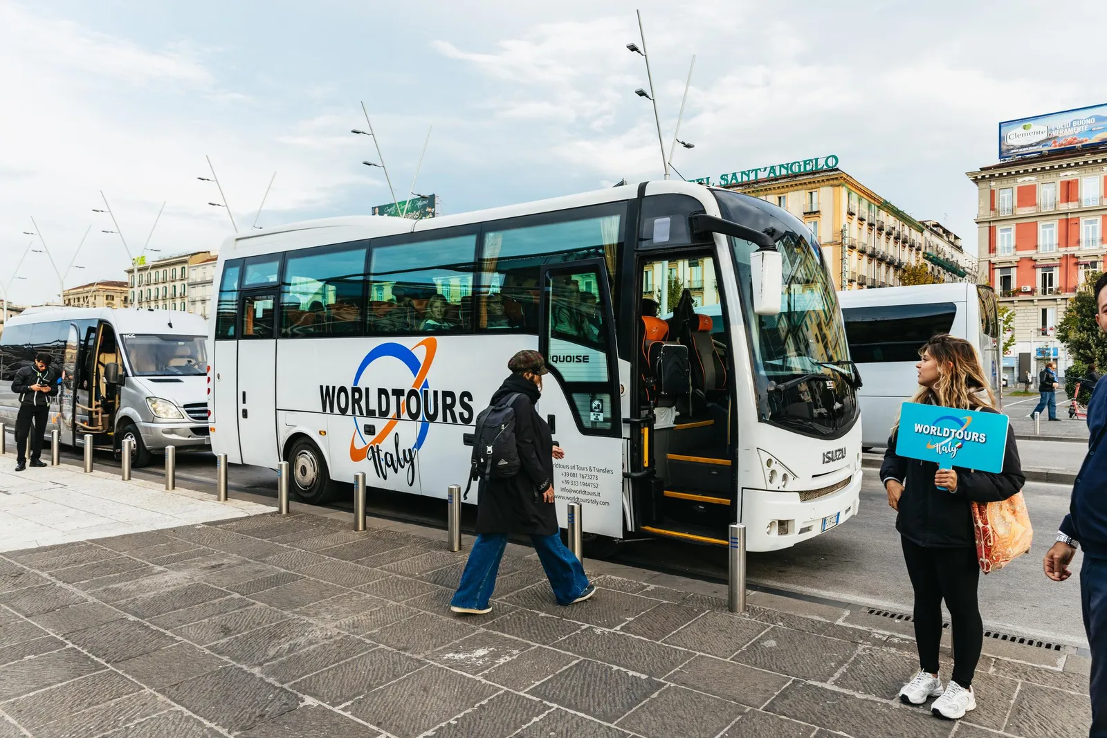White tour coach parked on a city street while a guide holds a sign beside it
