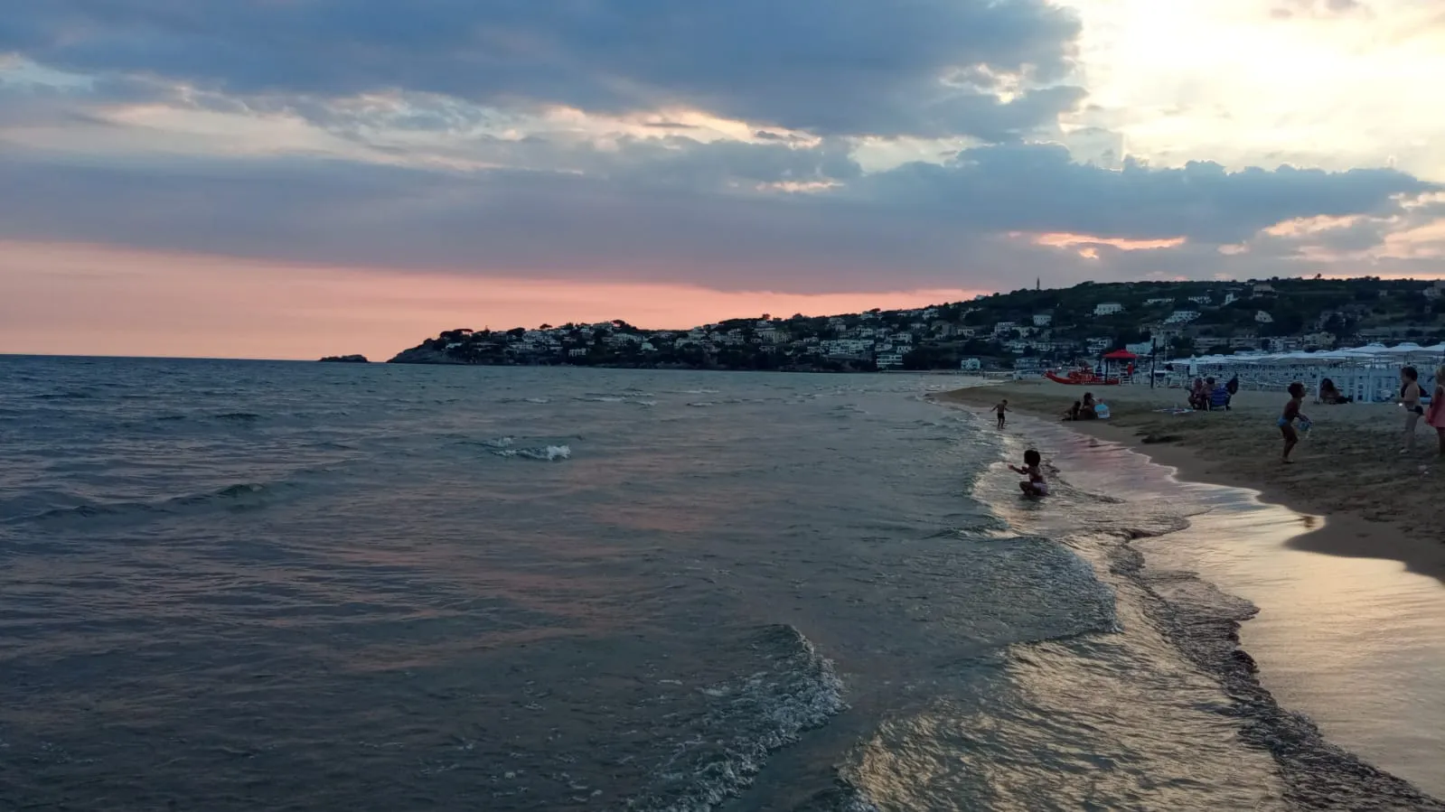 Sandy beach and calm sea at dusk under a cloudy pink and grey sky