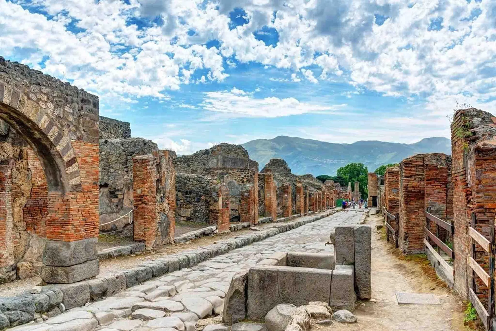 Paved Roman street at Pompeii with brick walls, stepping stones and a mountain beyond
