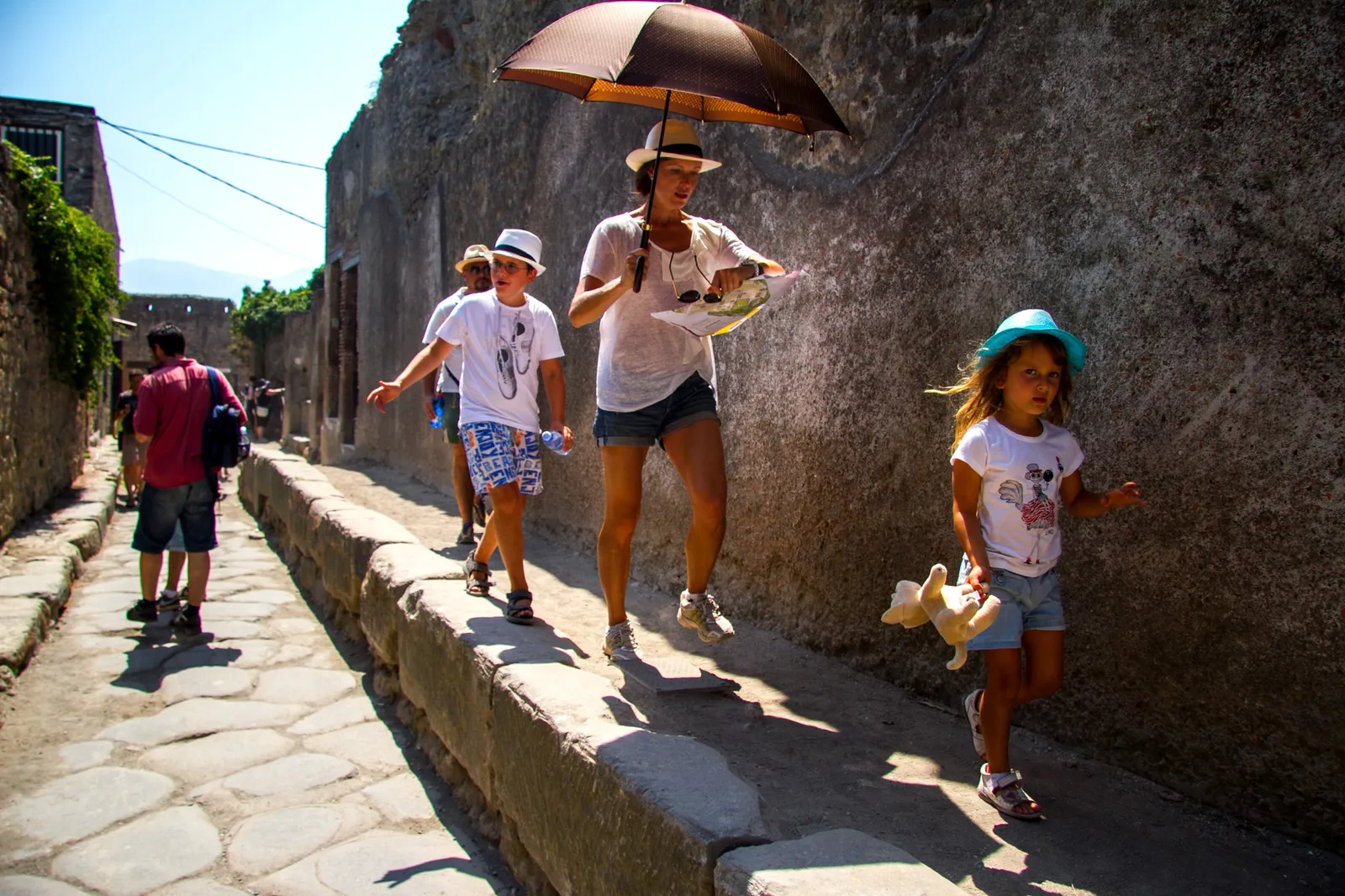 Family and a woman with an umbrella walking along a Pompeii street