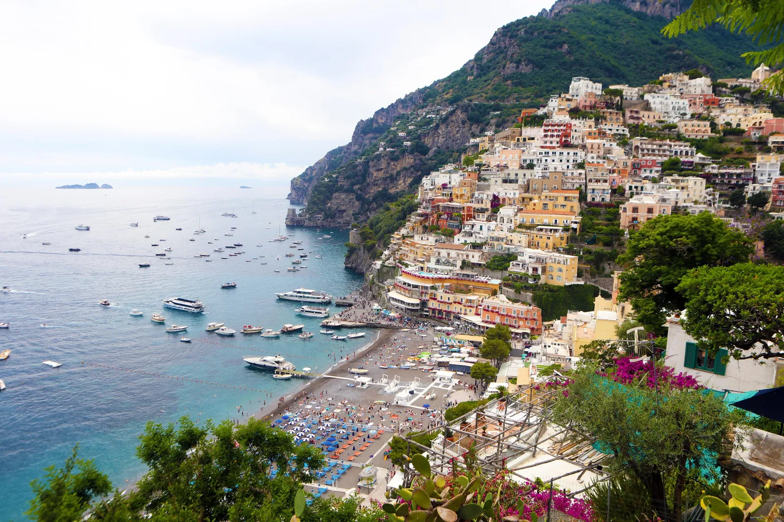 Positano's houses and a crowded beach beside a bay dotted with boats