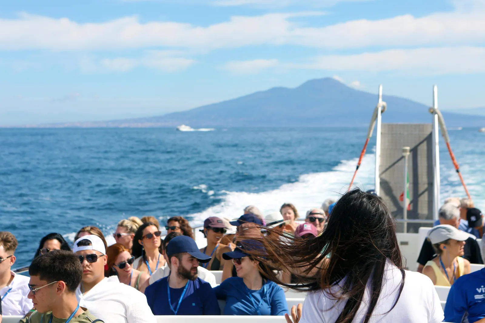 Passengers on a boat deck with Mount Vesuvius across the bay