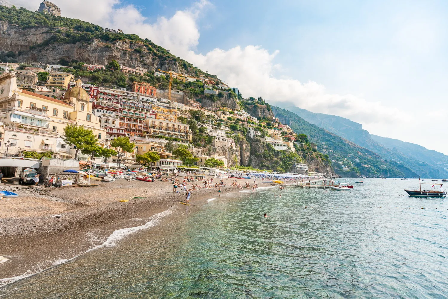 Pebble beach and shallow clear water below a hillside of terraced buildings