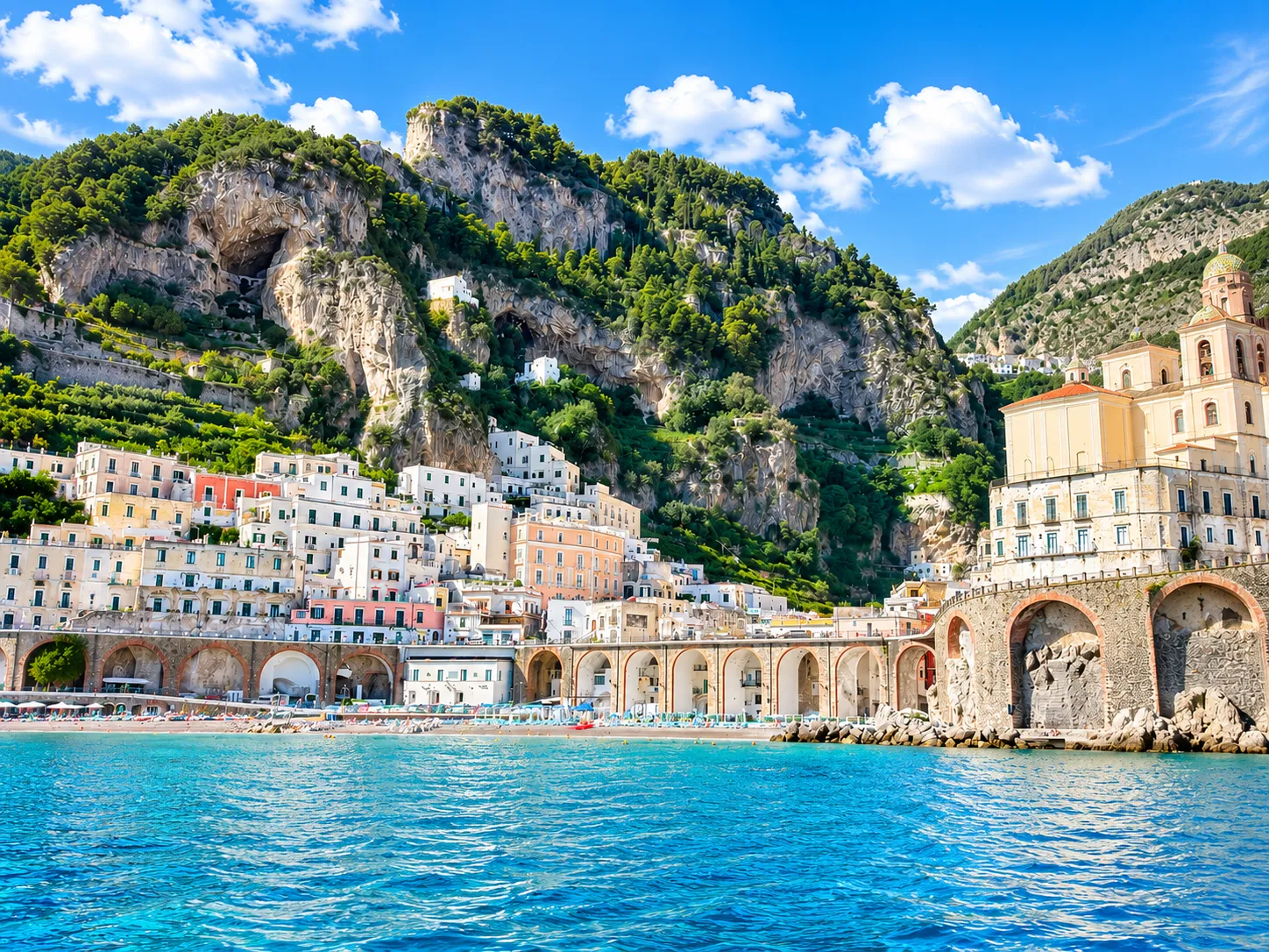 Amalfi coast village with a church tower and arched waterfront beneath rocky cliffs