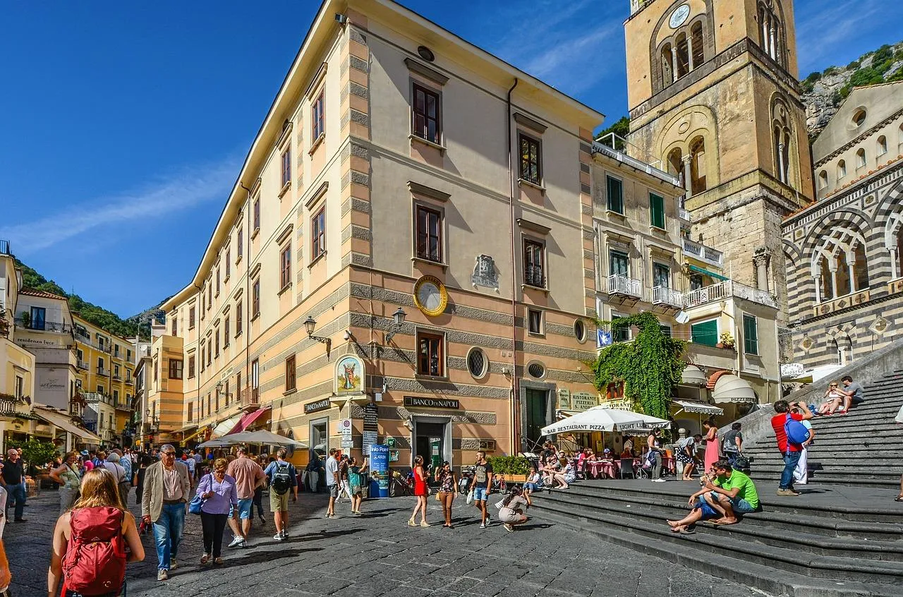 Crowded town square with cafe tables and a stone stairway leading up to a church