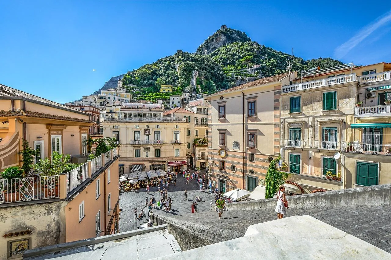 Town square and pastel buildings below a steep green mountain, seen from above