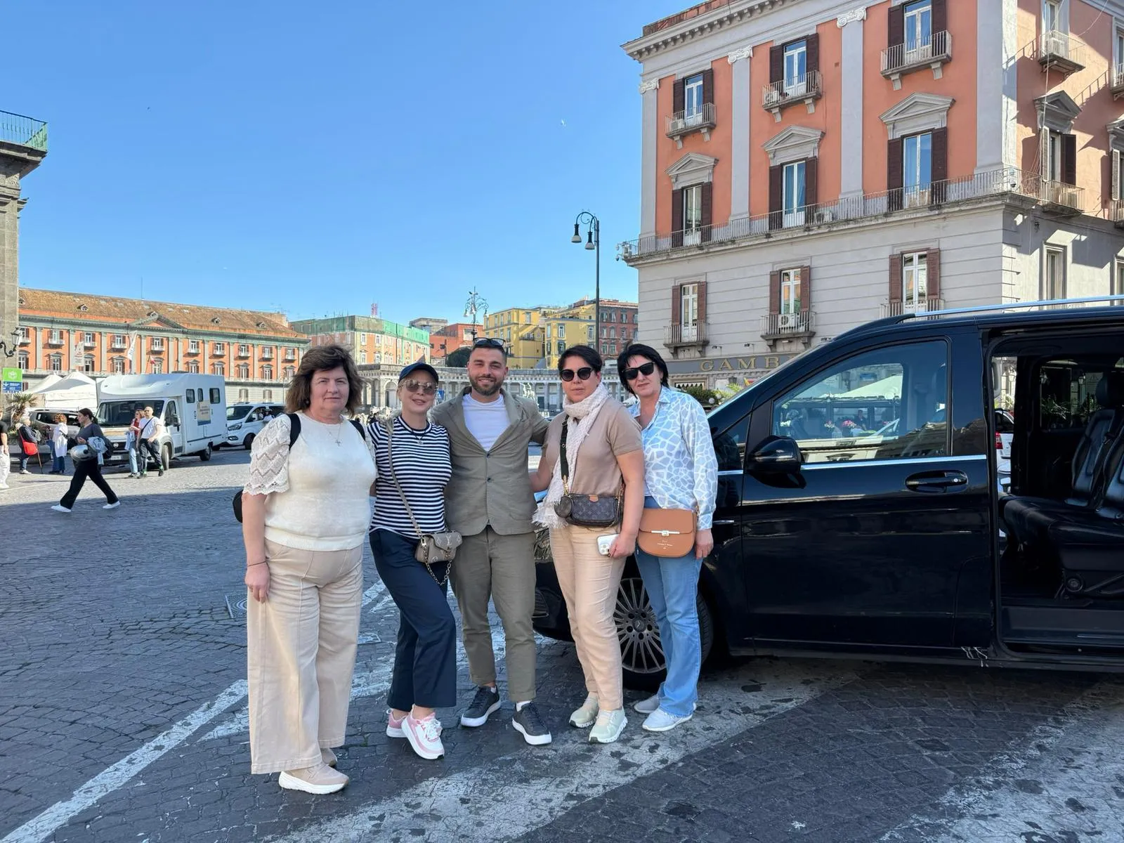 Five people standing beside a black minivan on a city square