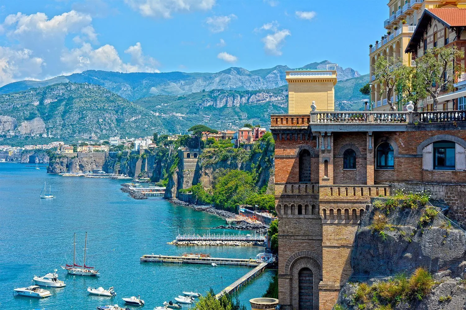 Sorrento's harbour with sailboats, a pier and brick buildings on the cliff top