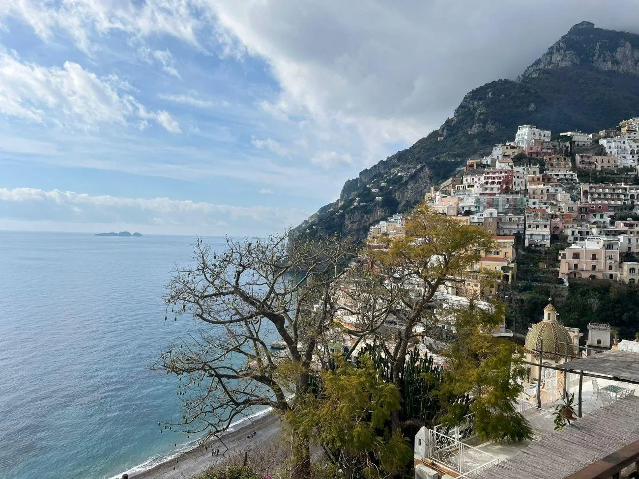 Hillside village with a domed church above the sea, seen through bare branches