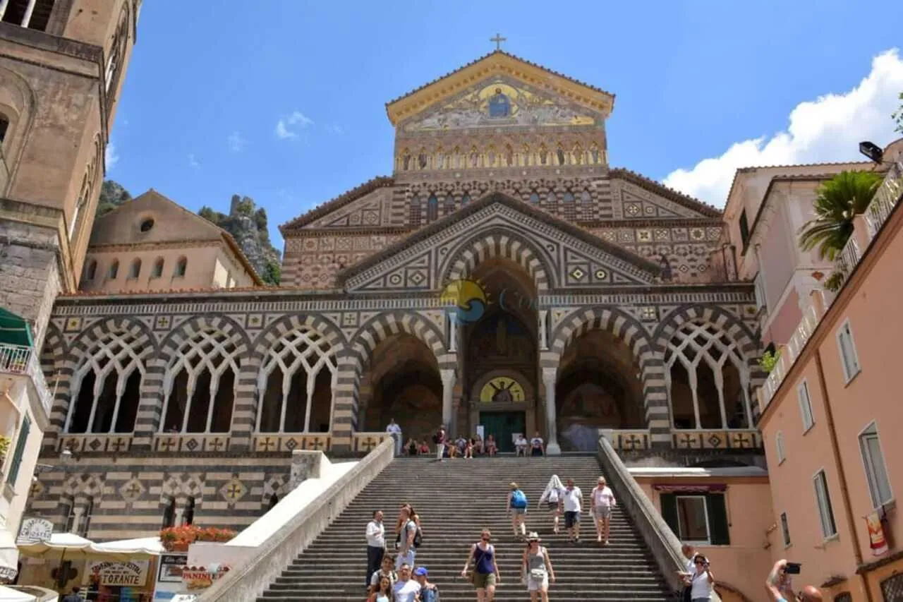 Amalfi cathedral's striped facade above a wide stairway with visitors