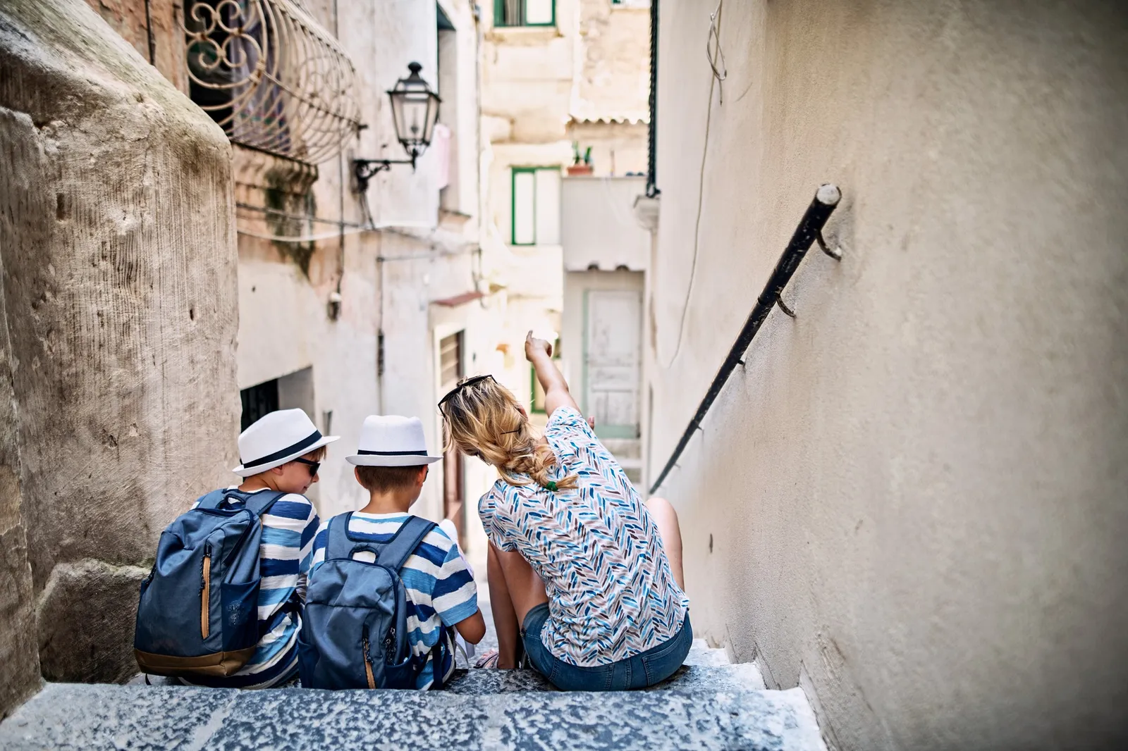 Adult and two children in sun hats sitting on steps in a narrow whitewashed alley