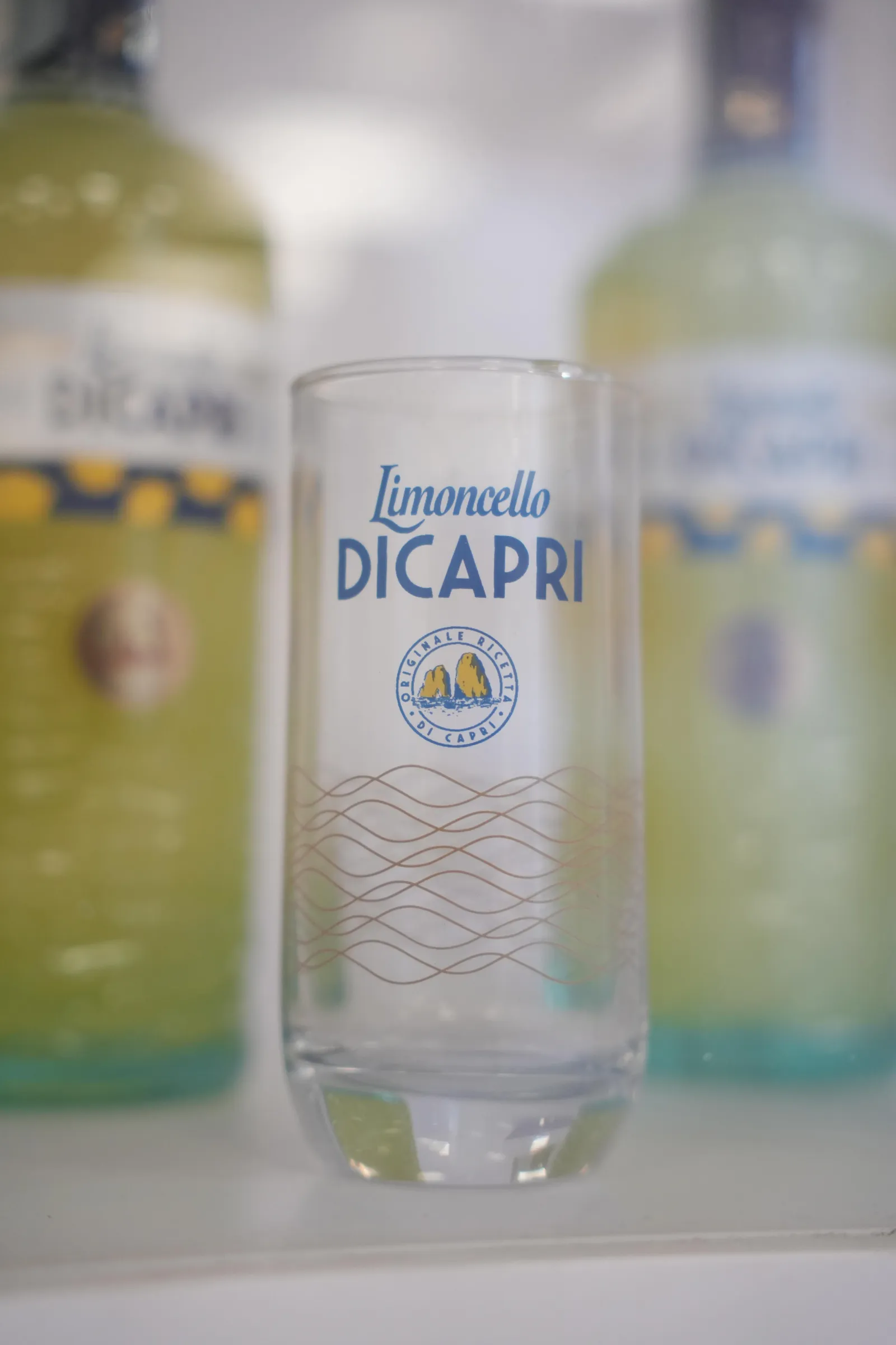 Limoncello bottles and a tall glass on a shelf