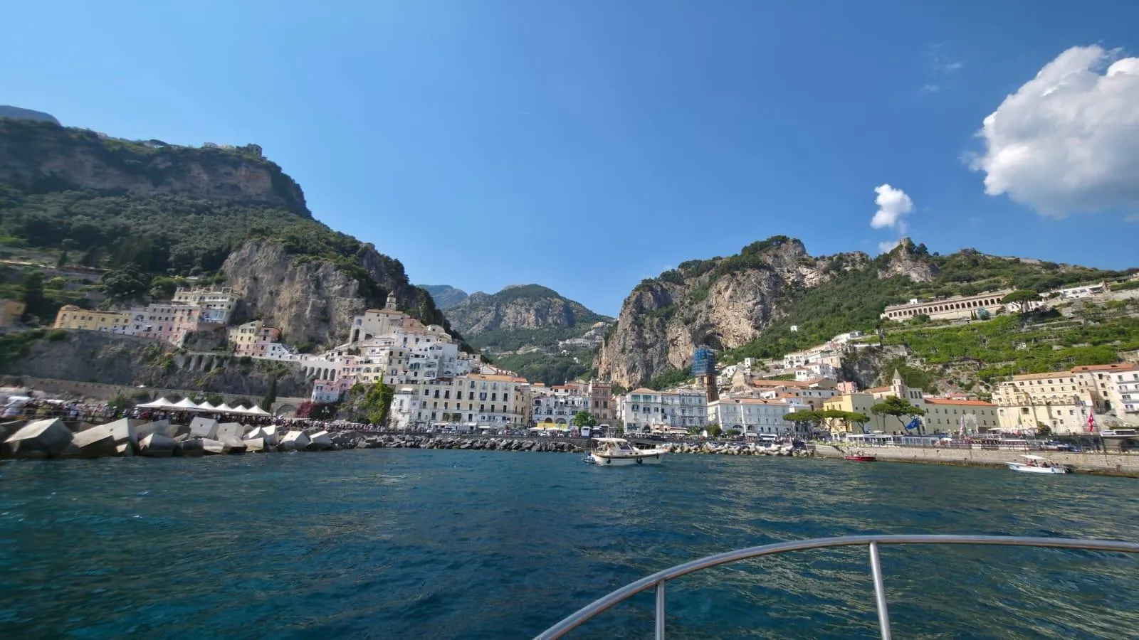 Amalfi's harbour and houses below rocky mountains, seen from the bow of a boat