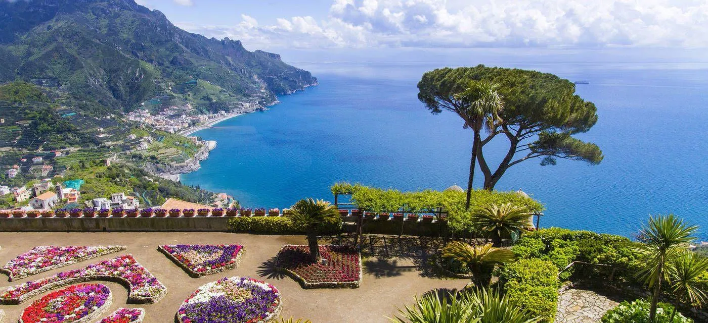 Flower beds and an umbrella pine on a garden terrace above a blue bay