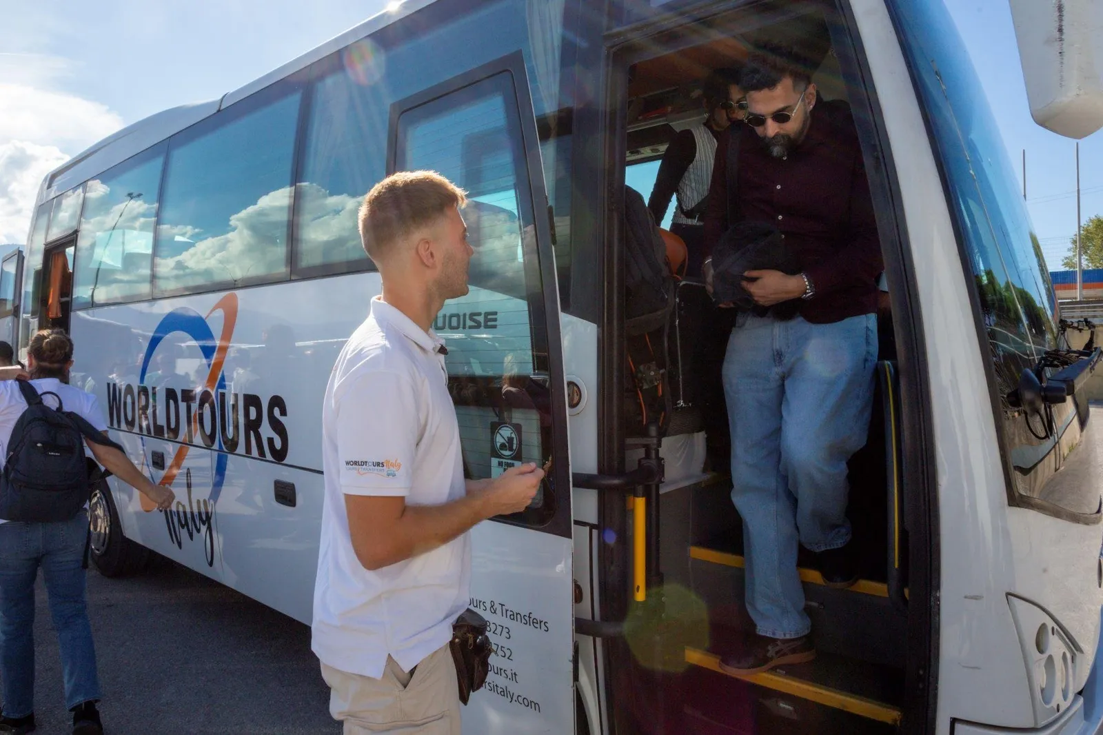 Guide in a white shirt beside a tour coach as passengers step off