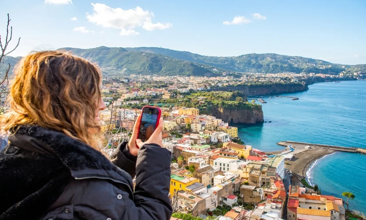 Woman photographing Sorrento's rooftops and a cliffside coast with her phone