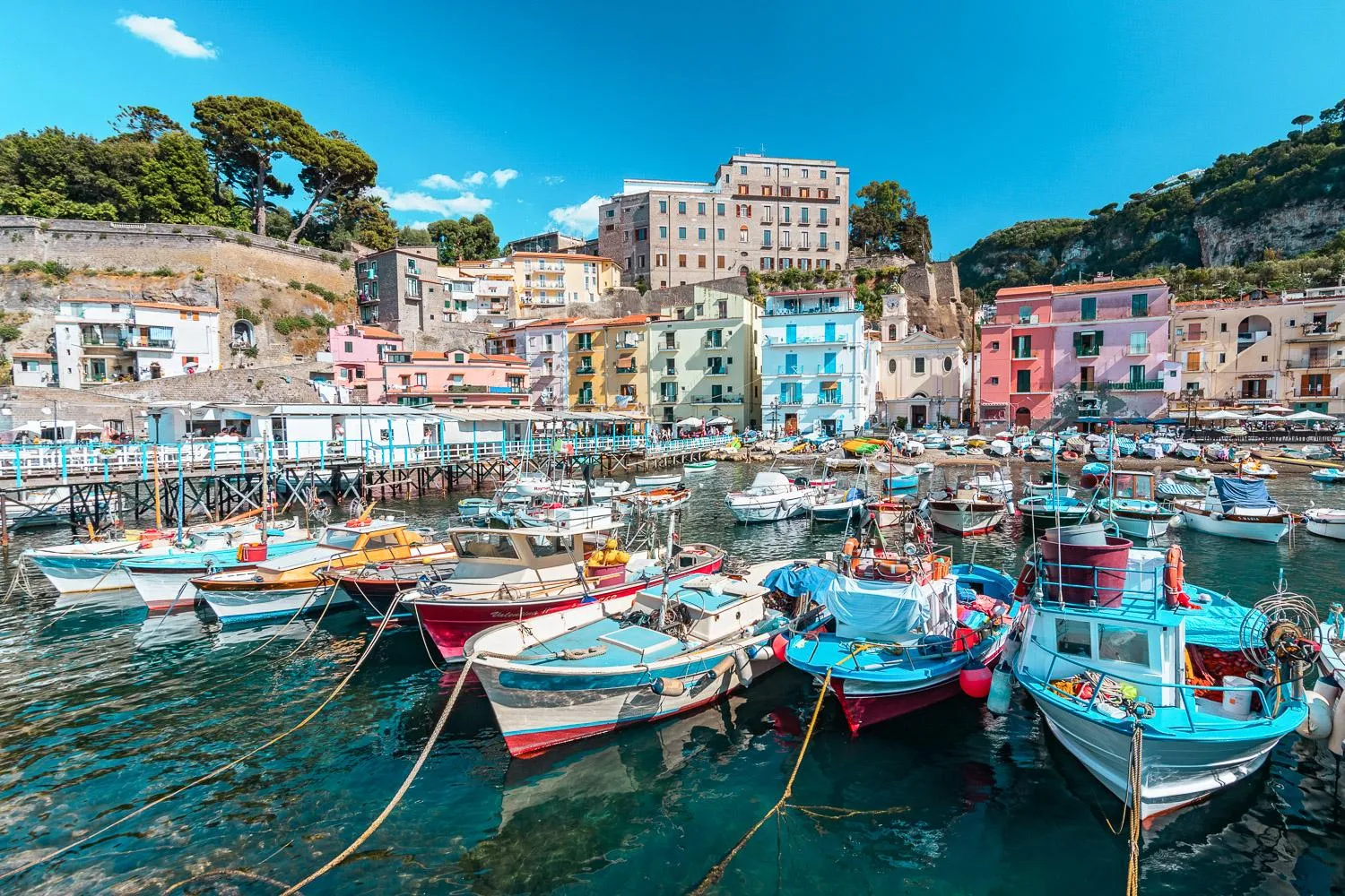Small colourful fishing boats moored in a harbour below pastel waterfront buildings